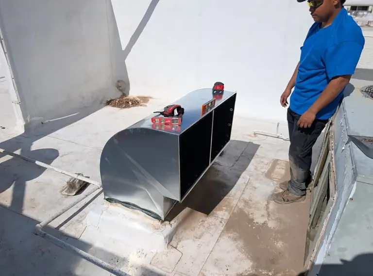 Technician next to a rooftop duct transition on a commercial roof in Tempe, AZ